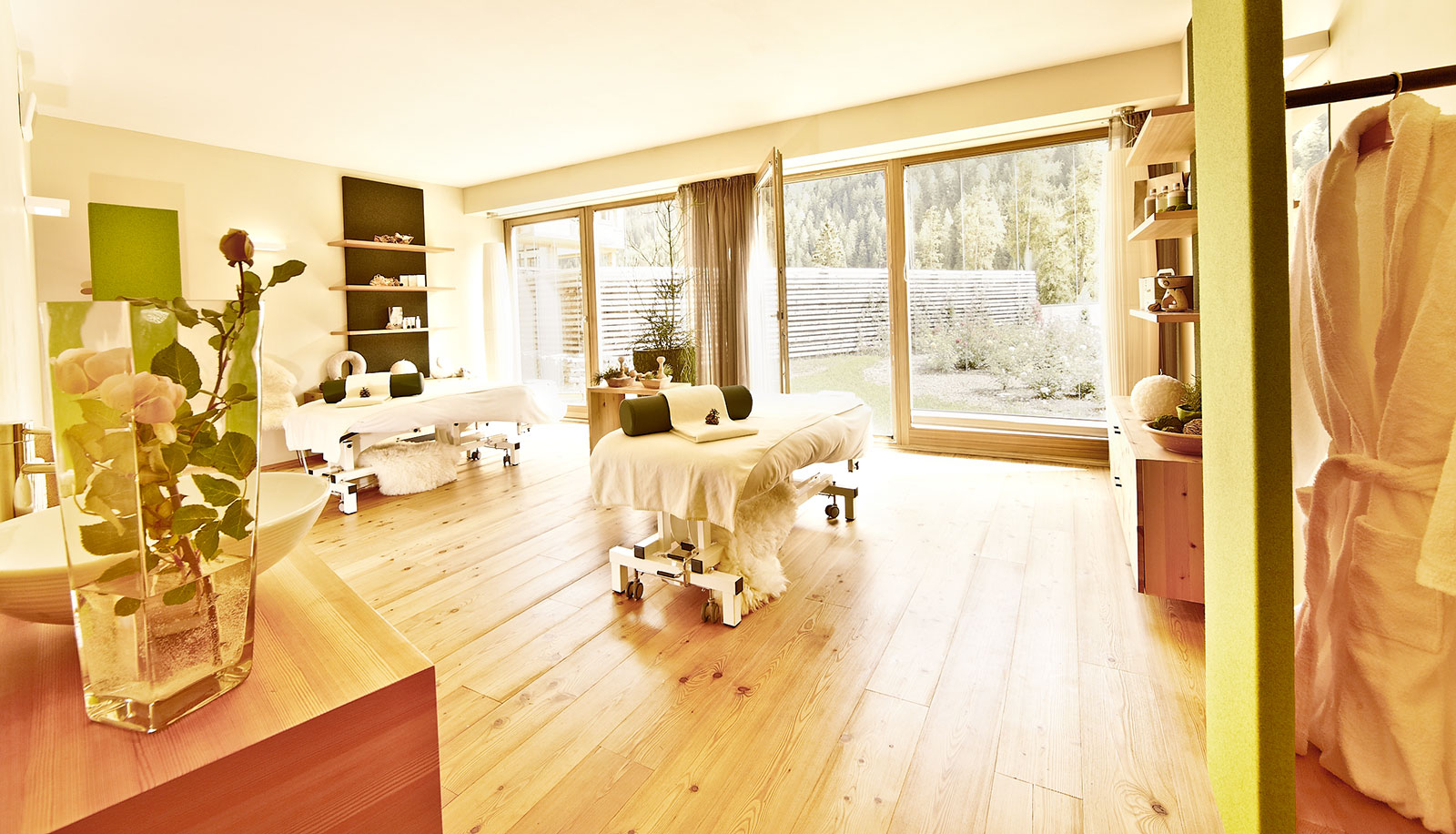 Stanza trattamenti dell'hotel Arosea in Val d'Ultimo con lettino per massaggi, pavimento in legno e vista sul giardino