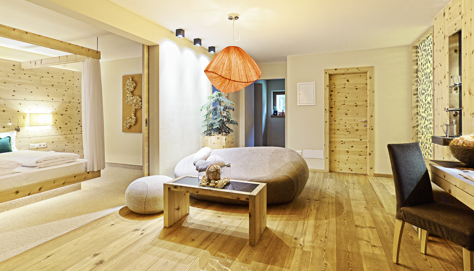 Eine Suite des Arosea Life Balance Hotels im Ultental mit Holzboden, Design-Sofa und Doppelbett im Hintergrund