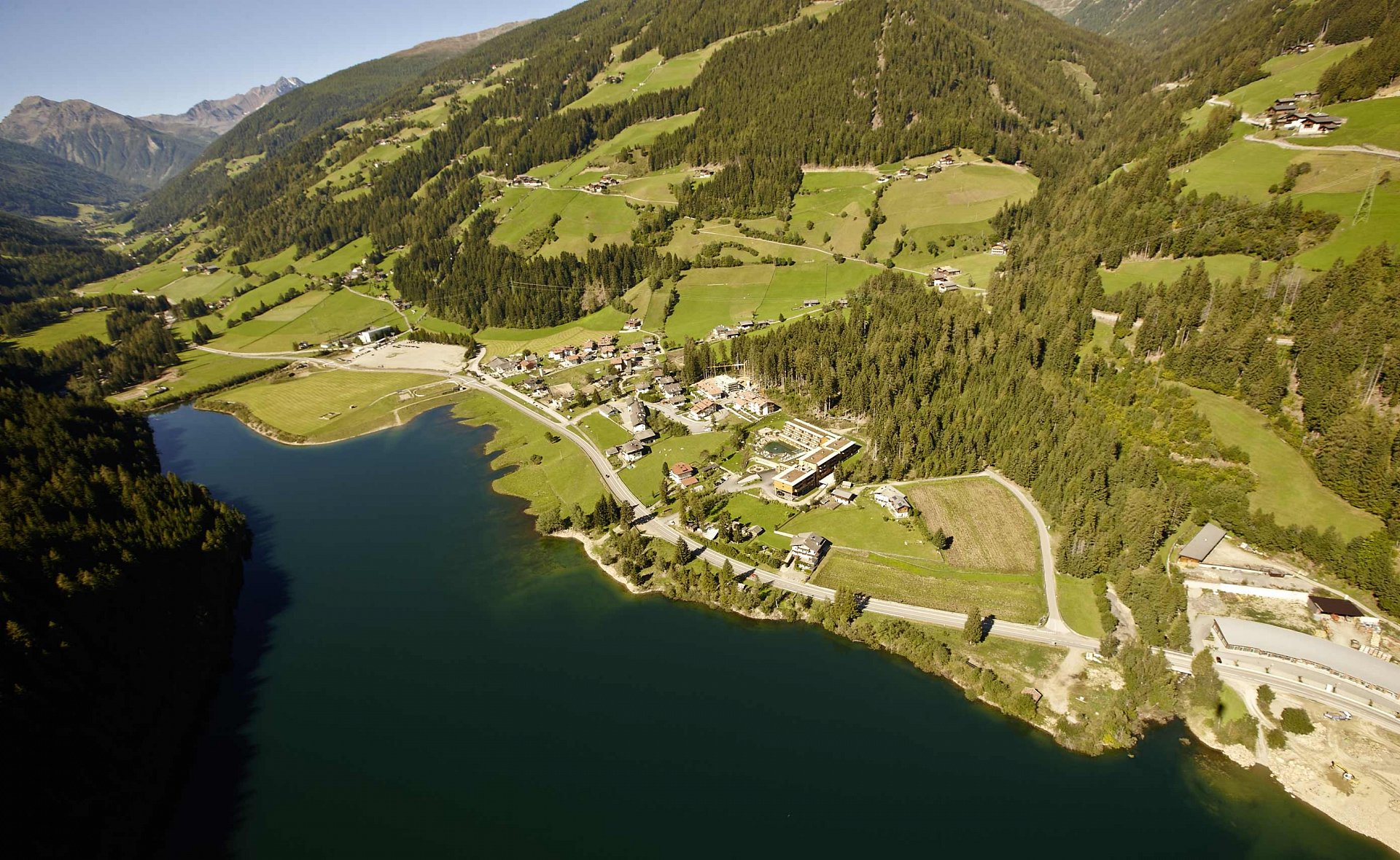 Der Zoggler Stausee mit Kuppelwies am Ufer und den Bergen im Hintergrund