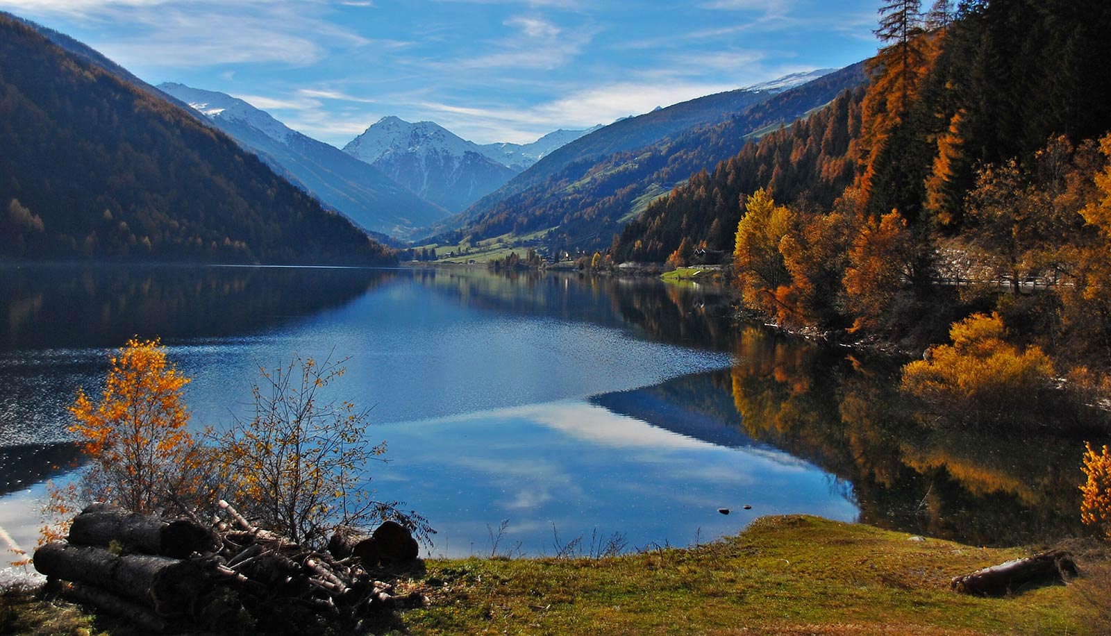 Der Zoggler Stausee im Ultental im Herbst mit verschneiten Bergen im Hintergrund