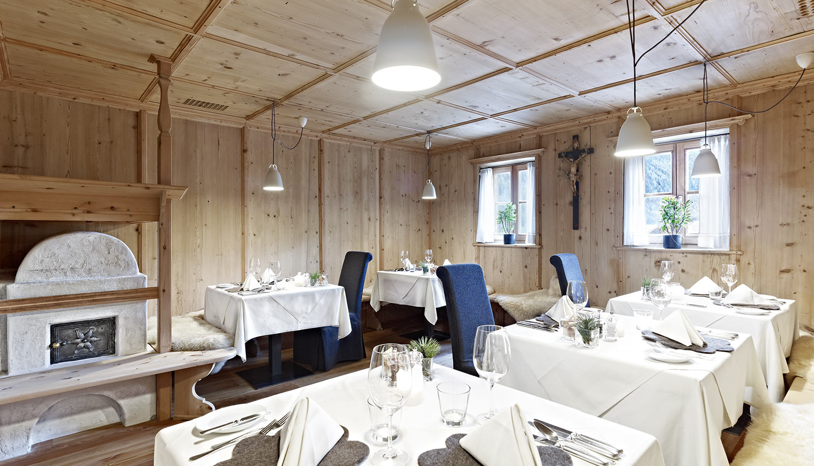 Stube in legno chiaro con stufa e tavoli apparecchiati all'Arosea Life Balance Hotel in Val d'Ultimo